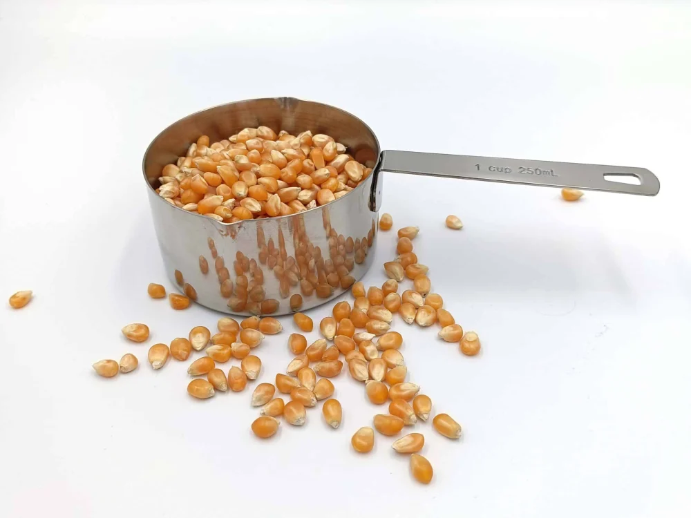 Edelstahl-Messbecher mit 250 ml Füllvolumen, gefüllt mit Popcornmais, auf weißem Hintergrund.